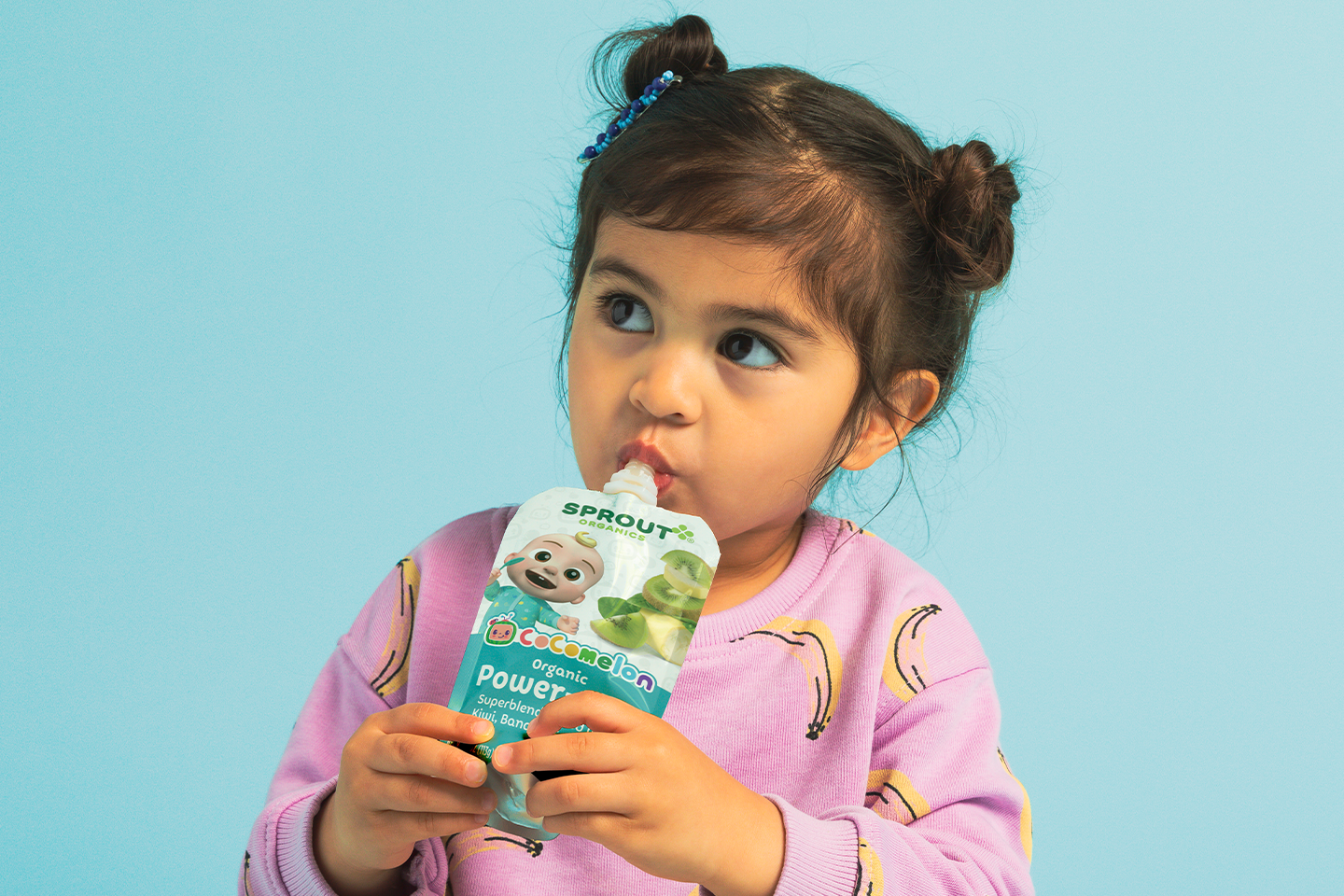 toddler on a blue background eating a food pouch