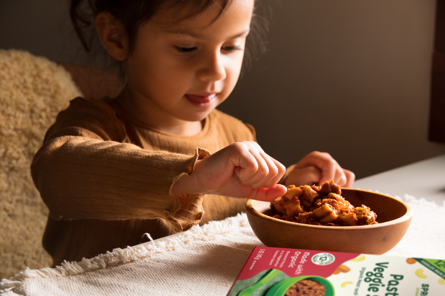 A toddler self feeding themself the pasta and veggie sauce organic toddler meal